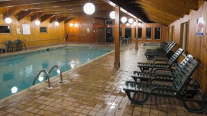 Una piscina interior con suelo de baldosas, paredes de madera y varias sillas de descanso.
