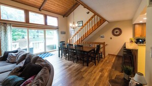 Un amplio salón con escalera de madera, una mesa de comedor con sillas y una zona de cocina.