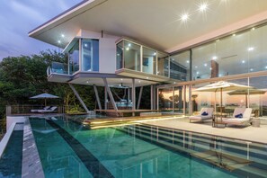 A modern house with a glass-enclosed upper level, a swimming pool, and outdoor seating with umbrellas. - This exquisite villa will give you the best sunset view! Dont miss out! (Liberia)