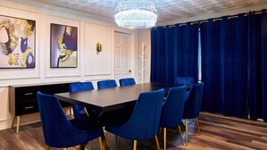 Ein Esszimmer mit einem dunklen Holztisch, blau gepolsterten Stühlen und einer Kristallleuchter.