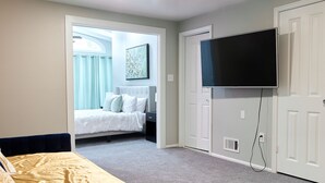 Ein Schlafzimmer mit einem Bett, einem an der Wand montierten Fernseher und einer Tür zu einem anderen Raum.