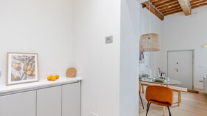 Una cocina moderna con armarios blancos, un comedor con una mesa redonda y sillas naranjas, y un techo con vigas de madera a la vista.