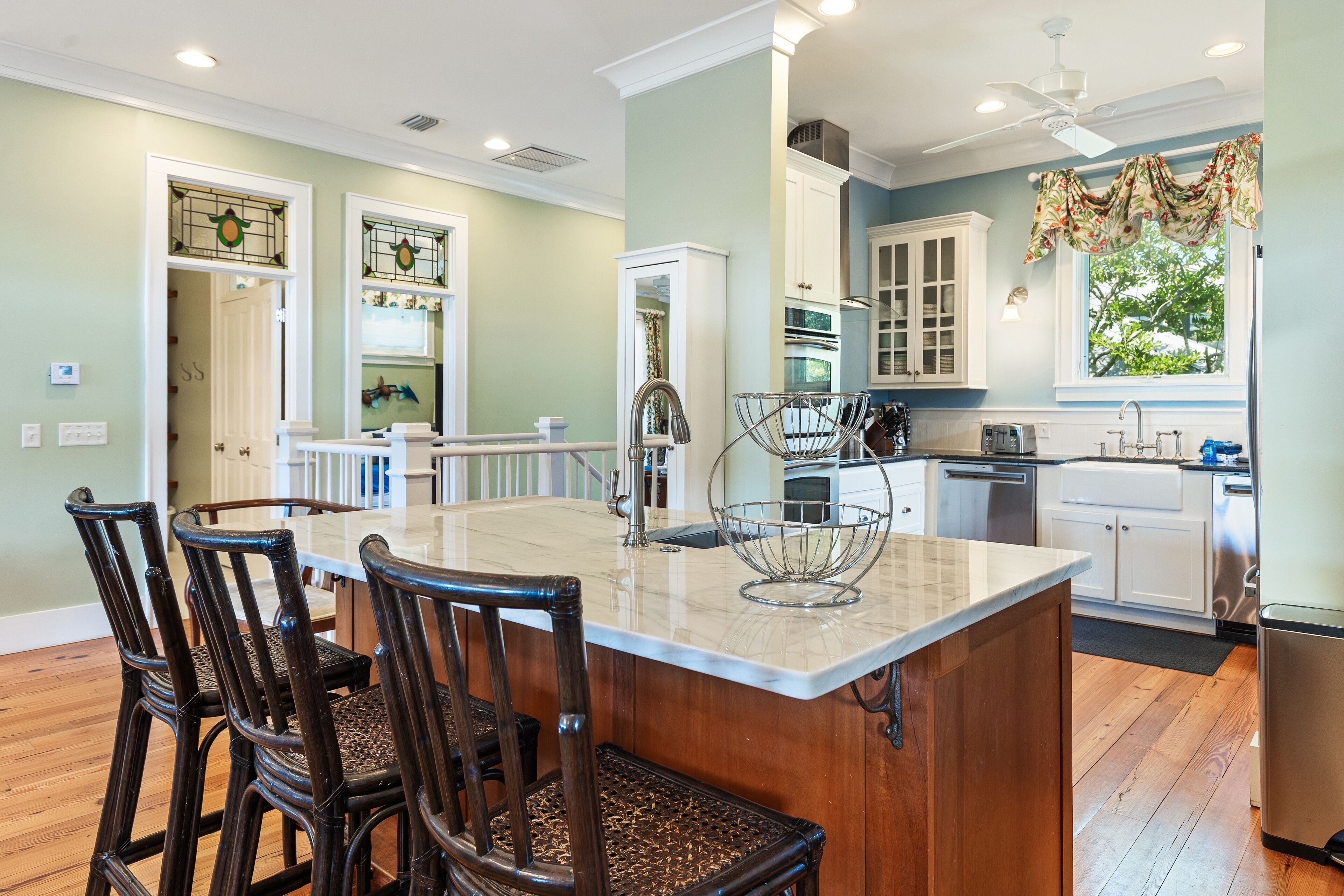 A kitchen with a central island, wooden chairs, white cabinets, and a window with a view of greenery.