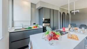 A modern kitchen with a central island, stainless steel appliances, and a variety of fruits and bread on the counter.