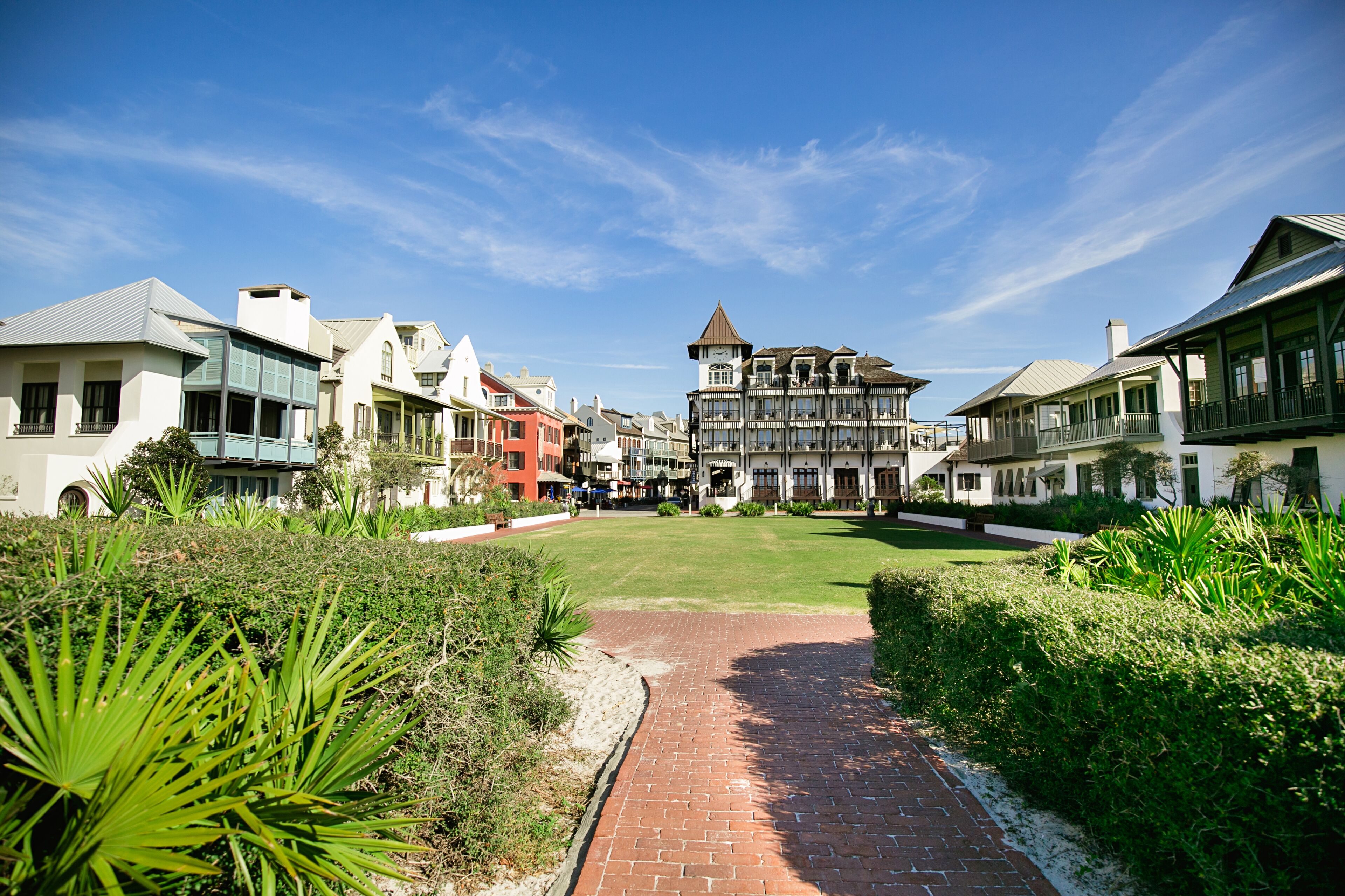 A pathway leading to a building with a central tower, surrounded by lush greenery and other buildings.