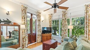 A living room with a ceiling fan, a television, a wooden cabinet, and a sofa. - Gulfside Rosemary "Freedom Carriage House" |Studio |Sleeps 4 | 2 Bikes (Rosemary Beach)