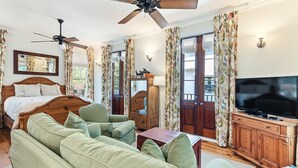 A bedroom with a bed, a green sofa, a wooden cabinet with a TV, and a ceiling fan. - Gulfside Rosemary "Freedom Carriage House" |Studio |Sleeps 4 | 2 Bikes (Rosemary Beach)