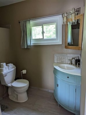 A bathroom with a toilet, sink, and window. - The Greenland Motel - Room No. 7 (Munising)