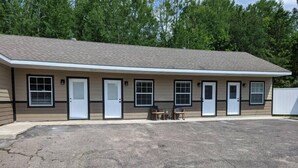 A single-story motel with a flat roof, multiple entry doors, and a parking lot. - The Greenland Motel - Room No. 7 (Munising)