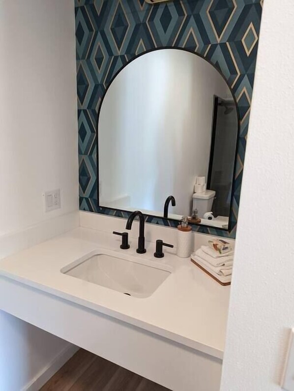 Un baño con un lavabo blanco, grifos negros y un espejo grande.