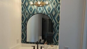 A bathroom with a white vanity, a large mirror, and a geometric patterned backsplash. - The Greenland Motel - Room No. 7 (Munising)