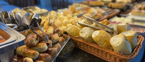 A buffet with various baked goods, including rolls and bread, and utensils like tongs and forks.