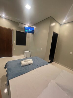 Une chambre d’hôtel avec un lit, un téléviseur fixé au mur, un petit climatiseur et une porte.
