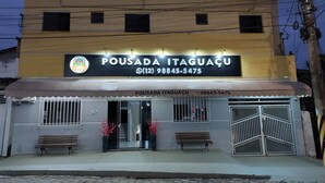 A building with a sign reading "POUSADA ITAGUACU" and a phone number. There are two benches outside and a gated entrance. - Pousada Itaguaçu (Aparecida)
