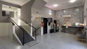 A spacious lobby with a staircase, a reception desk, and a stone wall. - Pousada Itaguaçu (Aparecida)