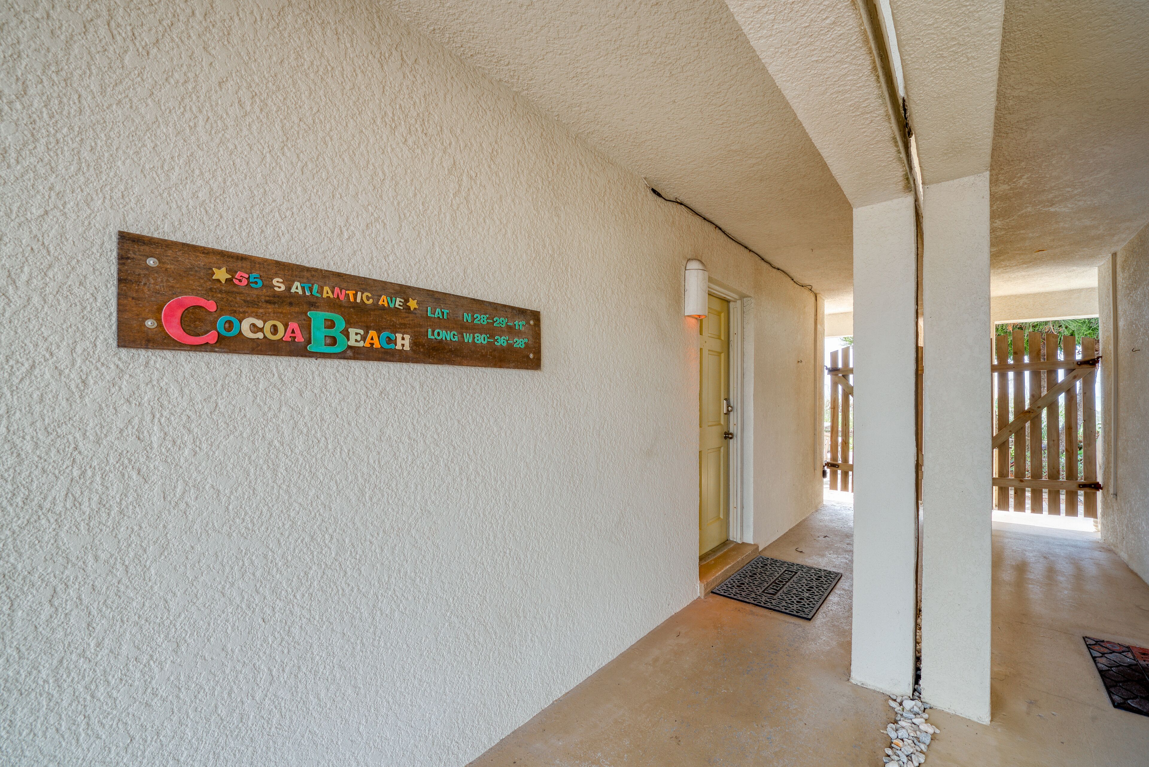 Corredor com placa de madeira indicando a localização do quarto Cocoa Beach, uma porta e cerca de madeira ao ar livre.