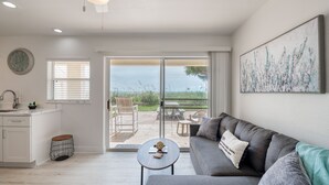 Una sala de estar moderna con un sofá gris, una mesita redonda y vistas al exterior a través de amplios ventanales correderas.