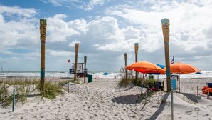 Una playa arenosa con postes de madera, sombrillas y una torre de salvavidas.