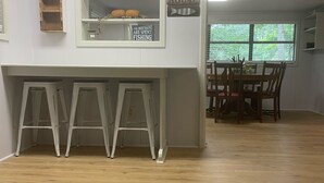 A room with a wooden floor, a white wall with a clock, a shelf with a bird and a welcome sign, and a dining area with chairs and a table. - Quiet Lakefront Cottage (Zwolle)