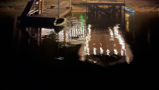 A wooden gazebo with string lights, a dock, and a boat on a calm body of water surrounded by trees. - Quiet Lakefront Cottage (Zwolle)