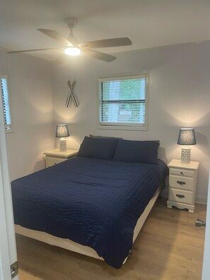 A bedroom with a bed, two bedside tables with lamps, a ceiling fan, a window with blinds, and a door. - Quiet Lakefront Cottage (Zwolle)