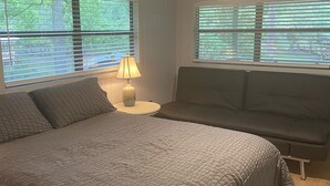 A bedroom with a bed, a nightstand, a lamp, a ceiling fan, and a window with blinds. - Quiet Lakefront Cottage (Zwolle)