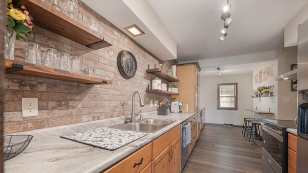 A modern kitchen with a brick backsplash, wooden shelves, and a stainless steel refrigerator.