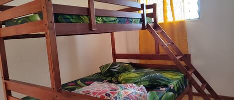 A bunk bed with a wooden frame, green bedspread, and a colorful pillow.