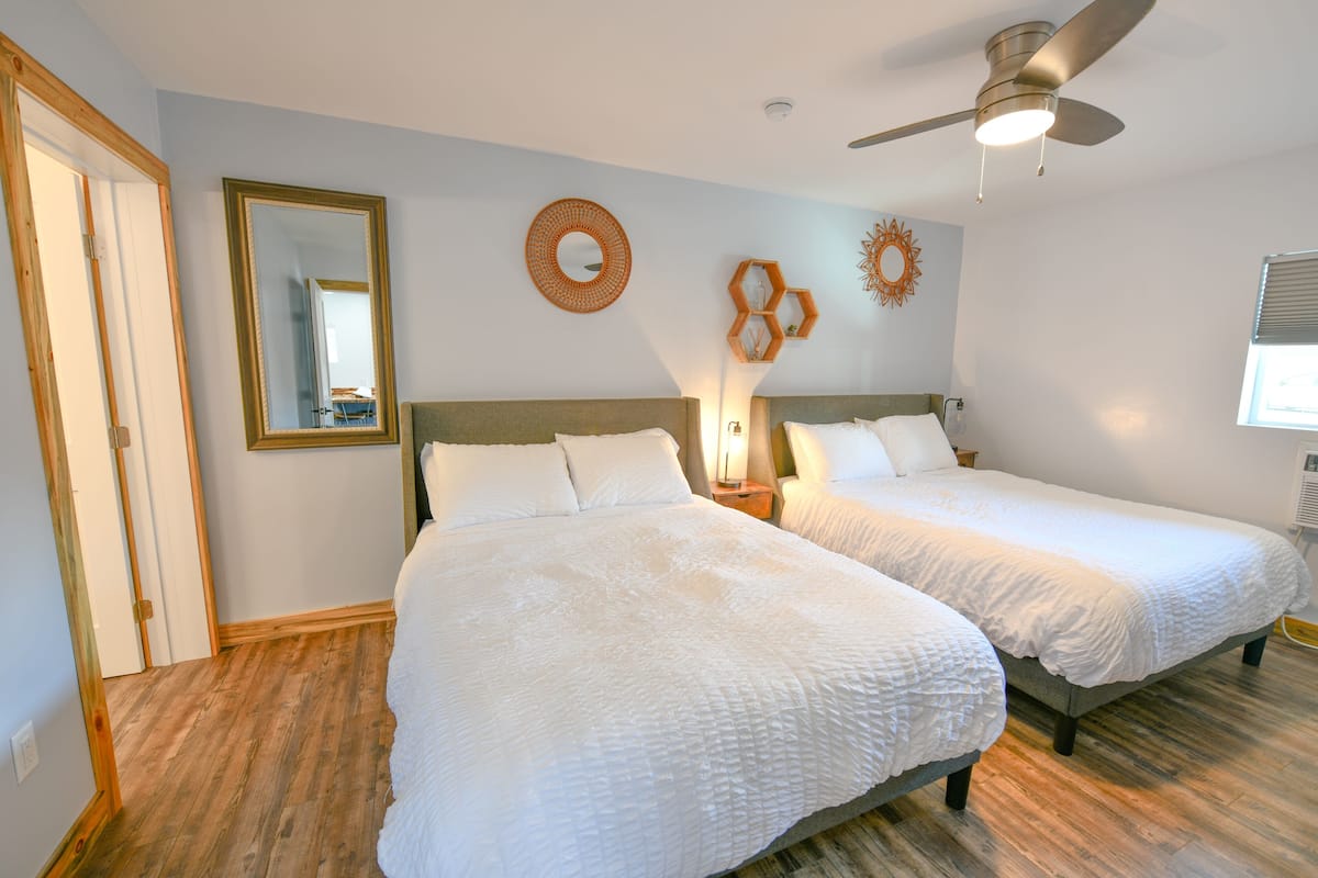 A bedroom with two beds, wooden flooring, a ceiling fan, and decorative wall art.