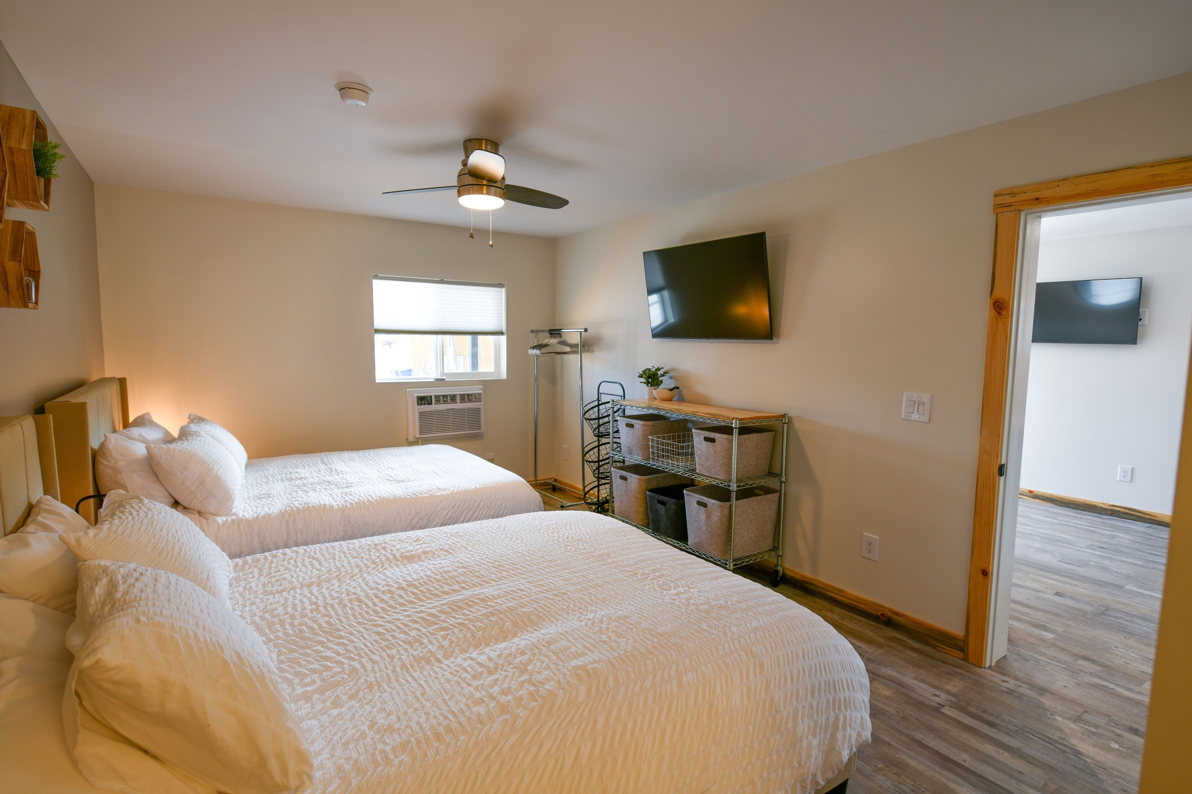 A hotel room with two beds, a ceiling fan, a TV mounted on the wall, and a window with blinds.