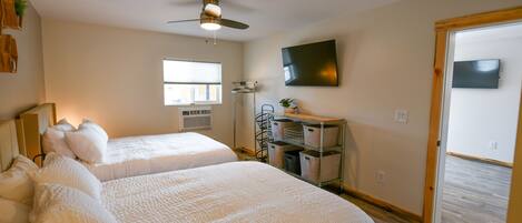 A hotel room with two beds, a ceiling fan, a TV mounted on the wall, and a window with blinds.