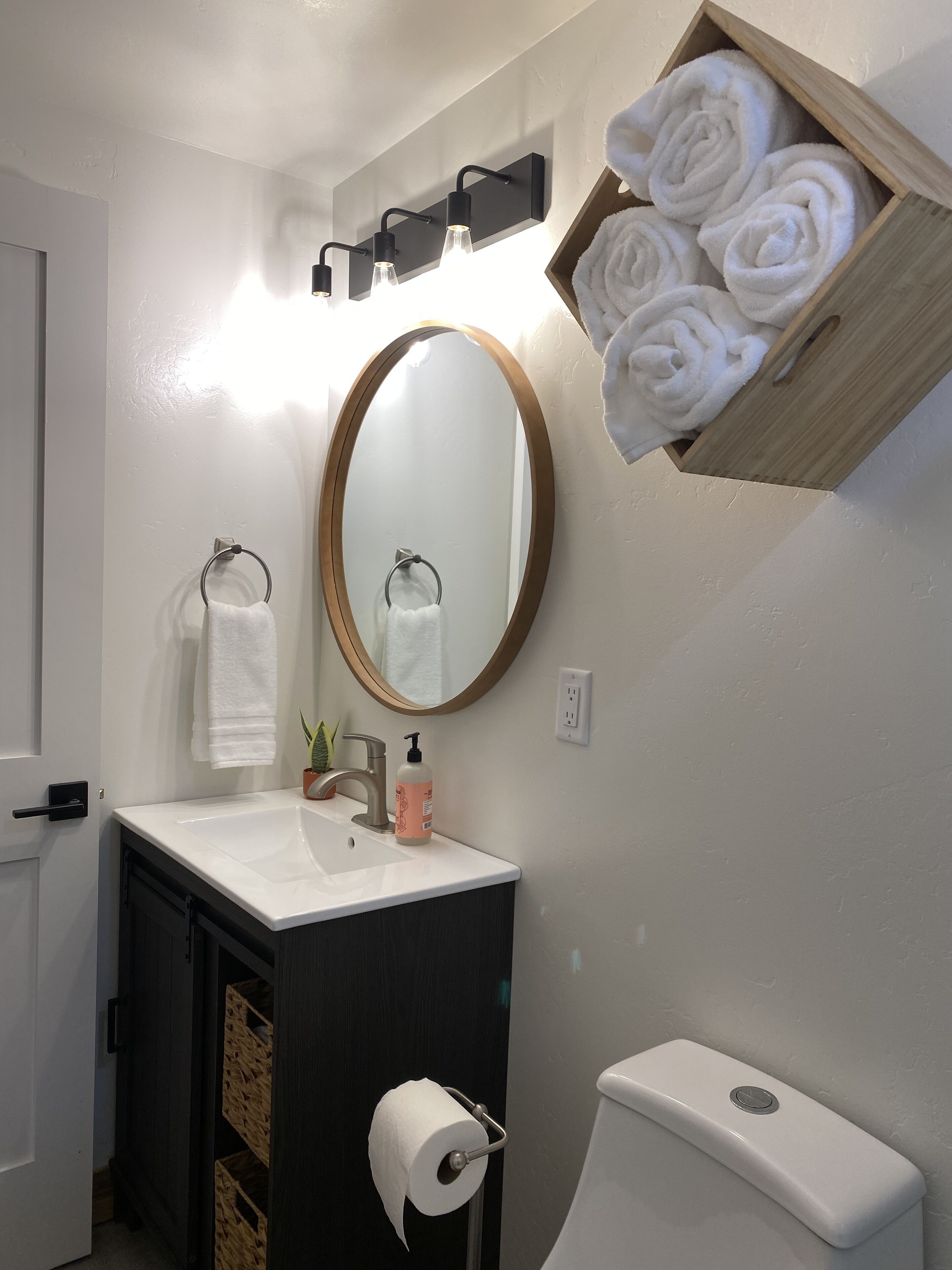 A bathroom with a white sink, a round mirror, a wooden towel rack, and a toilet.