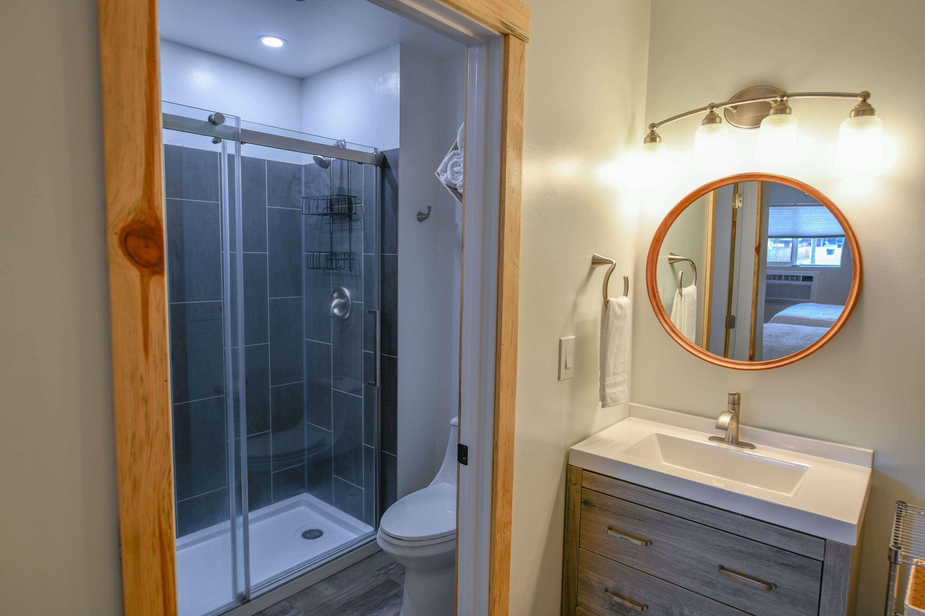 A bathroom with a glass shower enclosure, a toilet, a sink with a mirror, and wooden cabinetry.