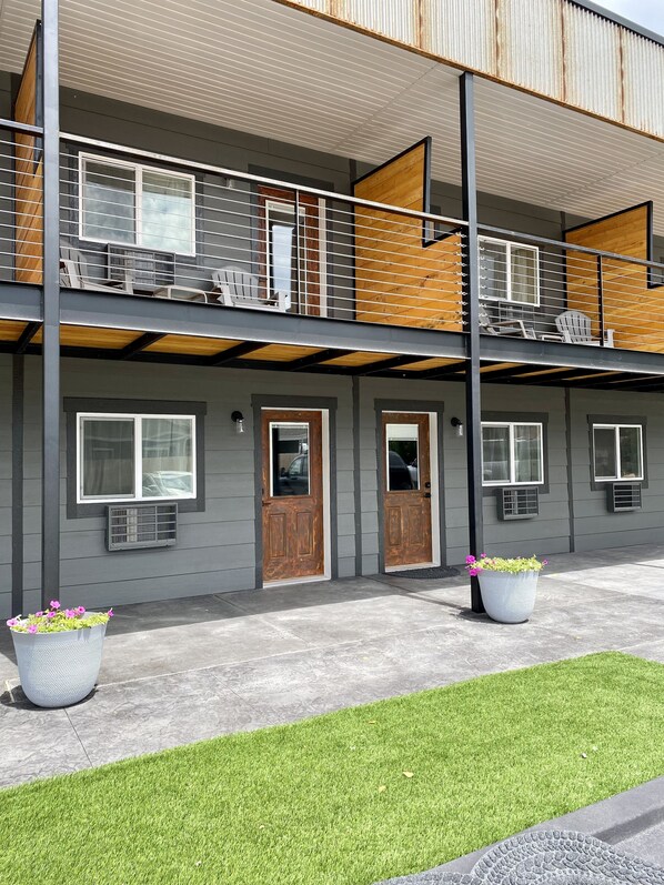 A two-story building with a balcony on the upper floor, a wooden door, and a small garden area with potted plants. - The Darmont Hotel and Suites (Darby)
