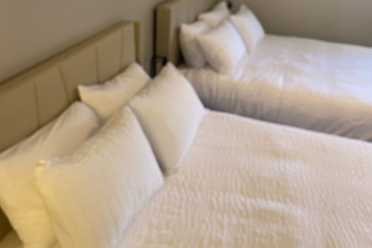 A hotel room with two beds, a headboard, and a wall-mounted shelf with decorative items.