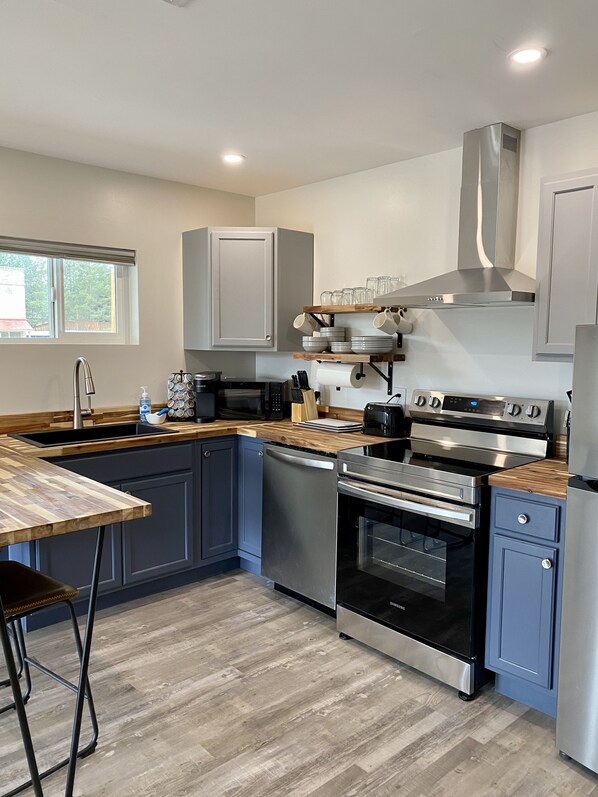 A modern kitchen with grey cabinets, stainless steel appliances, a wooden countertop, and a window providing natural light.