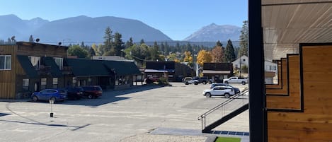 A parking lot with several cars, a building with a green roof, and mountains in the background.