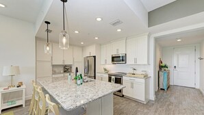 A modern kitchen with white cabinetry, granite countertops, stainless steel appliances, and a central island with bar stools. - Harbor Isle Fir, penthouse with views (Bradenton)