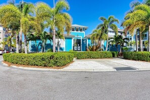 A hotel with a blue facade, palm trees, and a well-maintained hedge.