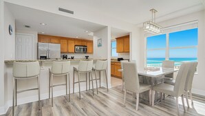 A modern kitchen with a central island, bar stools, and a dining area with a view of the ocean.