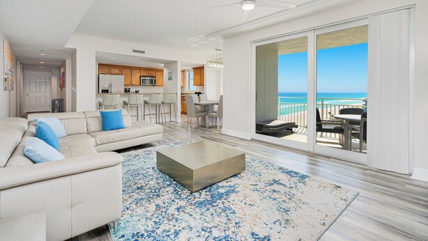 A spacious living room with a large sofa, a coffee table, and a view of the ocean through a sliding glass door.