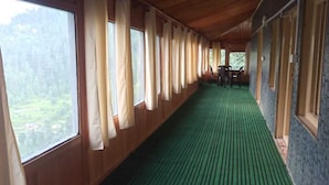 Un couloir aux murs en bois et aux grandes fenêtres, doté d’un sol recouvert de moquette et offrant une vue sur la verdure environnante.
