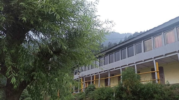 Un bâtiment à deux étages doté d’un balcon, entouré de verdure et d’un mur de pierre.