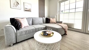 A modern living room with a grey sectional sofa, a white round coffee table, and a large window with blinds.