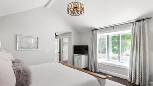 Un dormitorio con cama, televisor, ventana con cortinas y candelabro.