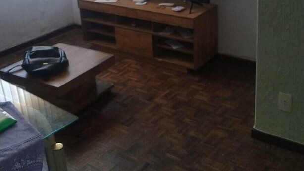 Un soggiorno con una grande televisione a schermo piatto su un supporto in legno, un tavolino da caffè in vetro e un pavimento in legno con un motivo a spina di pesce.