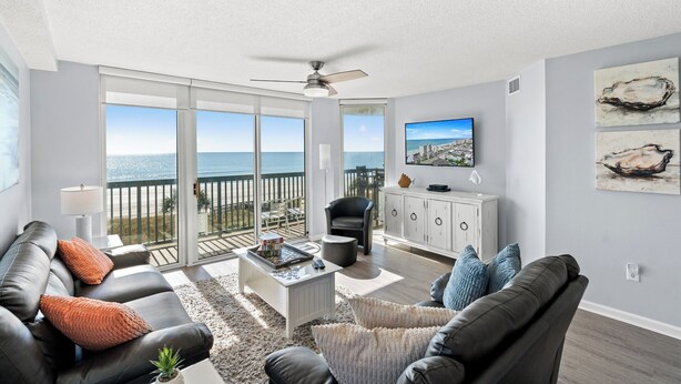 A modern living room with a large sliding glass door leading to a balcony with a view of the ocean. - Ashworth 309-Oceanfront 4BR Near Main Street, Pool (North Myrtle Beach)
