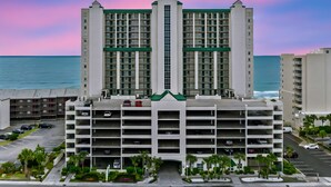 A multi-story parking garage with a central green roof, adjacent to a high-rise building with a symmetrical facade and a view of the ocean. - Ashworth 309-Oceanfront 4BR Near Main Street, Pool (North Myrtle Beach)