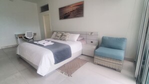 Una habitación de hotel con una cama, una silla, un escritorio con teléfono y un cuadro en la pared.