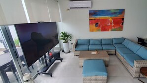 Una sala de estar con un televisor de pantalla plana grande, un sofá modular, una mesa de centro y un comedor con mesa y sillas.
